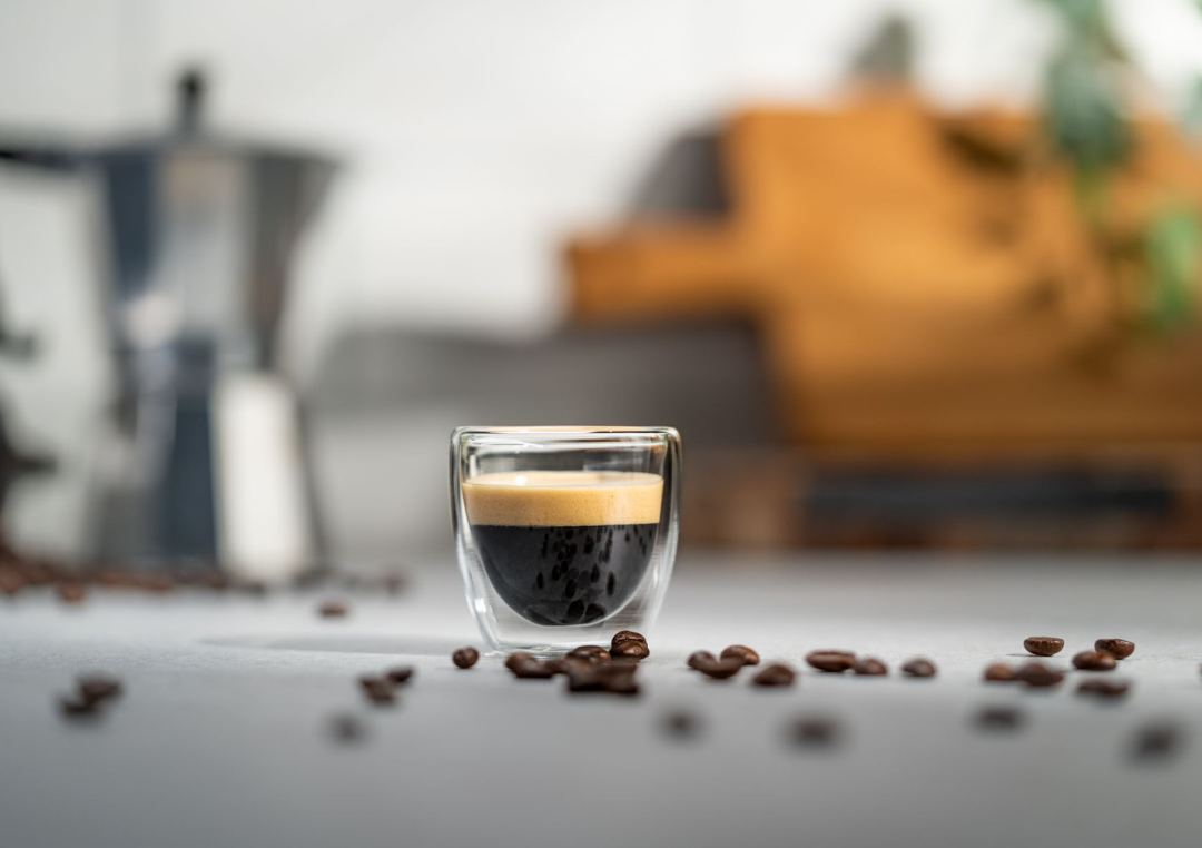 En kop espresso på et bord med kaffebønner liggende rundt om.