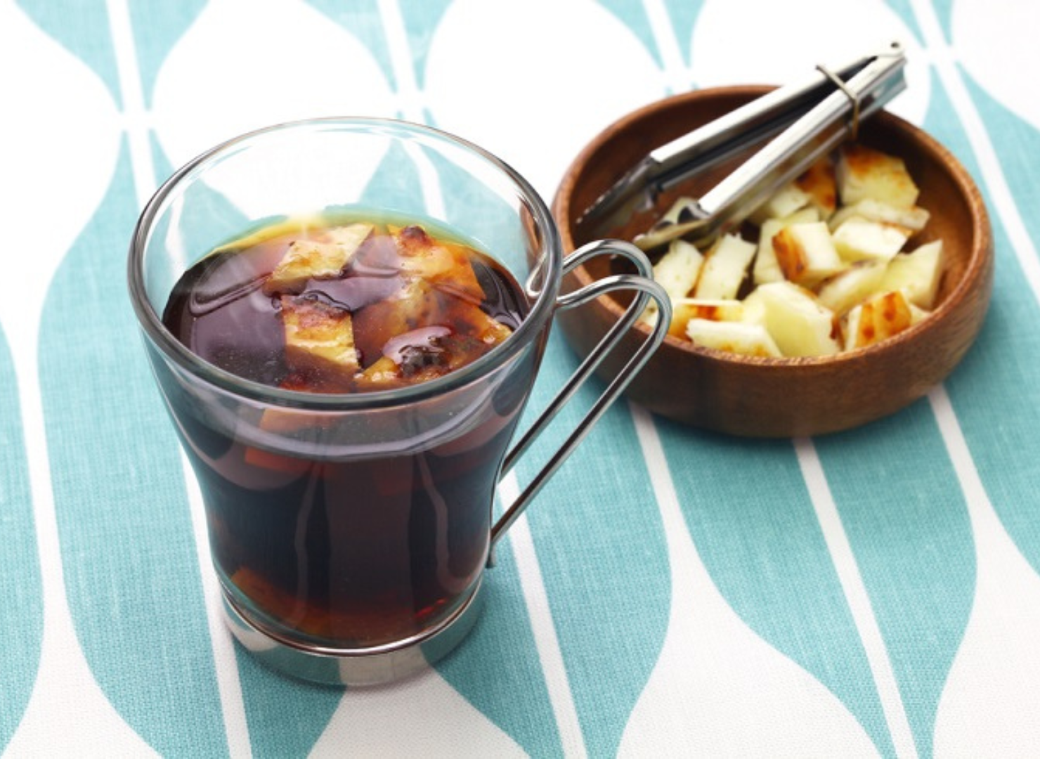 Et glas med sort kaffe på et bord med en skål med ost ved siden af