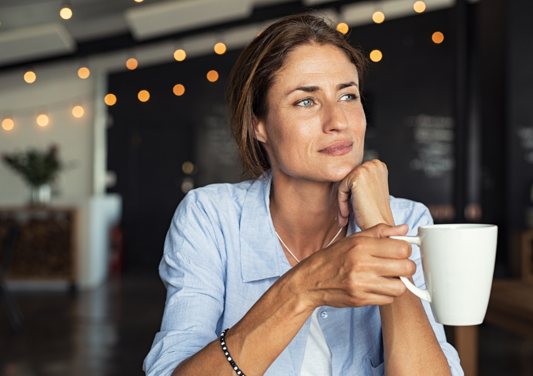 En kvinde i blå skjorte sidder med en kop kaffe i hånden